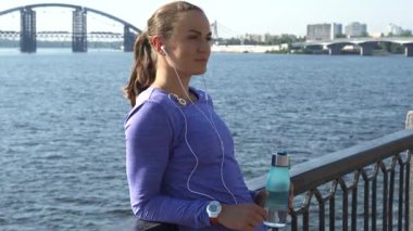 Genç, güzel bir kadın korkuluklara yaslanıyor, bir mp3 çalarda müziğinin keyfini çıkarırken manzaralı nehir kenarına bakıyor. Uzun, siyah saçları at kuyruğu ve canlı mor bluzuyla elinde su şişesiyle mutluluk saçıyor.