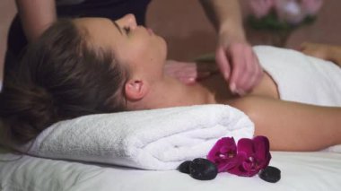 Uzun sarı saçlı sakin bir genç kız, narin nilüfer çiçekleri ve pürüzsüz taşlarla çevrili bir masaj masasının üzerinde rahatça yatıyor. Rahatlatıcı bir göğüs masajından, rahatlatıcı bir rahatlama ve huzurlu bir spa ortamından hoşlanır.