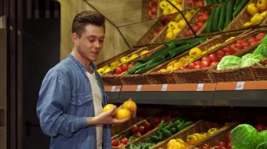Şık, sarışın, beyaz bir adam yoğun bir hipermarketten olgun domatesleri ve canlı dolgun dolma biberleri dikkatlice seçer. Sahne, alışveriş arabasını renkli ürünlerle doldururken sağlıklı yaşamın özünü yakalıyor.
