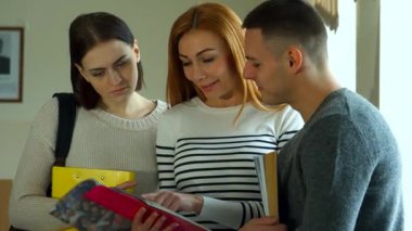 Canlı, kızıl saçlı bir kız öğrenci, her ikisi de canlı bir tartışmaya dalmış yakışıklı, esmer bir sınıf arkadaşına egzersiz defterini gösteriyor. Genç üniversite öğrencilerinin üçlüsü güneşli bir pencerenin yanında duruyor.