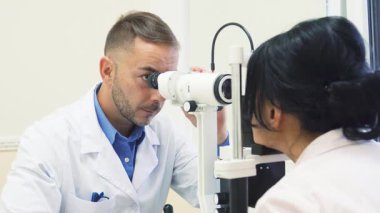 Parlak, iyi ışıklandırılmış bir ofiste odaklanmış bir göz doktoru, uzmanlaşmış bir cihaz kullanarak bir kadının gözlerini dikkatlice inceler. Özenli tavrı ve klinik yapısı göz sağlığının ve kişisel bakımının önemini vurguluyor.