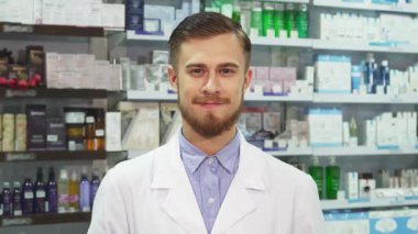 Dost canlısı genç bir eczacı canlı bir eczanede elinde iki paket renkli hapla güvenle duruyor. Parlak gülümsemesi, müşterileri bu iyi stoklanmış eczanede sağlık ve güzellik seçeneklerini keşfetmeye davet ediyor.