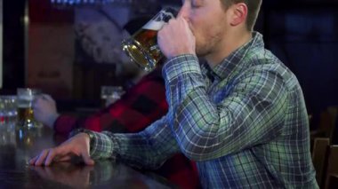 Yakışıklı kahverengi saçlı bir adam, canlı bir barda buzlu birasını kaldırırken neşeyle ışıldıyor. Bu çekici beyaz erkek, şık bir kareli gömlek giymiş, kutlamanın ve yoldaşlığın özünü canlı bir bar atmosferinde yakalıyor.