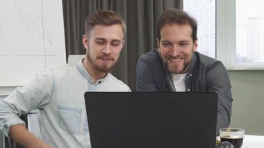 Yakışıklı genç bir iş adamı ve olgun erkek arkadaşı parlak bir dizüstü bilgisayardaki verileri incelerken neşeli bir tartışmayla meşguller. Gülüşleri profesyonelliği ve takım çalışmasını yansıtıyor, çağdaş ofis dekoruna karşı kurulmuş ve
