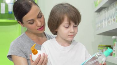 Neşeli bir anne ve sevimli oğlu eczanede enfes bir alışveriş deneyimiyle meşguller, iki canlı şampuan şişesini dikkatlice karşılaştırıyorlar. Küçük çocuk, ışıldayan bir gülümseme ile, renkli ürünler tarafından büyülenir,