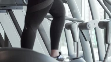 Şık spor kıyafetleri içinde enerjik ve iri yarı bir kadın eliptik bir antrenör üzerinde enerjik bir şekilde çalışıyor, pozitiflik ve kararlılık yayıyor. Yakın çekim, kardiyo rutinine dalarken yüzündeki neşe dolu ifadeyi yakalıyor.