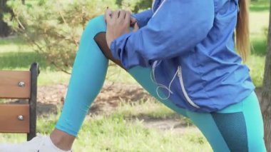 Kesilmiş bir atış, uzun ağaçlar ve benekli güneş ışığıyla çevrili canlı yeşil bir parkta gerinen kararlı bir atletik kadını yakalar. Bu ilham verici sahne, canlandırıcı bir açık hava antrenmanına hazırlanırken kendini spora adadığını gösteriyor.