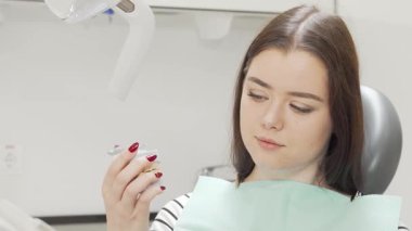 Gülümseyen neşeli bir kadın modern bir diş kliniğinde detaylı bir diş modelini tutuyor. Parlak ifadesi ve canlı diş çevresi, ağız sağlığı ve hasta bakımının önemini vurguluyor.