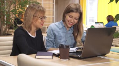 İki şık beyaz kız modern bir çalışma merkezinde dergilere göz atarken hararetli bir tartışma içindeler. Bir kız, şık gözlüklü, sayfaları hevesle çevirirken, diğeri, uzun kahverengi saçlı, dizüstü bilgisayarına odaklanıyor,