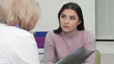 Odaklanmış genç bir kadın, elinde bir röntgen görüntüsü tutarken doktorunu dikkatle dinliyor. Bu sahne, tıbbi ortamlarda iletişimin ve anlayışın önemini vurgulayarak sağlık hizmetinin özünü yakalıyor.