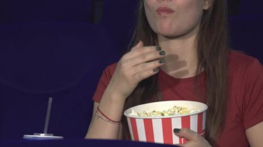 Neşeli genç bir kadın lüks bir sinema koltuğunda oturur ve filme dalmışken klasik çizgili kovadan patlamış mısırın tadını çıkarır. Uzun, koyu renk saçları omuzlarının üzerinde dalgalanır ve canlı gülüşü saf bir zevk yayar. Bu da film deneyimi yaratır.