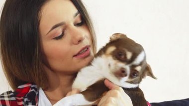 Güzel genç bir kadın evinde rahat bir şekilde oturup sevimli köpeğini sıcacık kucaklıyor. Yumuşak, sevgi dolu etkileşim neşe saçıyor. Nazik gülüşü ve köpeklerin neşeli ifadesi sevgi dolu bir sahne yaratıyor.
