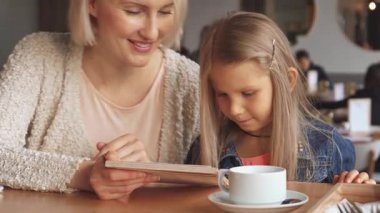 Neşeli bir sarışın anne ve sevimli kızı rahat bir kafede içki seçmeye dalmışlar. Küçük kız menüdeki en sevdiği seçeneğe hevesle işaret ederken, annesi sıcak bir şekilde gülümsüyor, samimi bir bağ kurma anı yaratıyor.