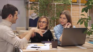 Kafkasyalı genç bir adam, modern bir çalışma merkezindeki dizüstü bilgisayarında ilginç bir şey gösteriyor. Çekici esmer adam ve gözlüklü şık sarışın kadın ekranı hareketli bir şekilde işaret ederken, güzel kahverengi saçlı kadın...