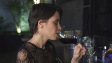 Çekici, genç, esmer bir kadının kendine güveni ve cazibesi ile şık bir barda bir kadeh şaraptan keyif aldığı büyüleyici bir yakın plan. Neşeli gülüşü ve gevşek tavırları davetkar bir atmosfer yaratıyor.