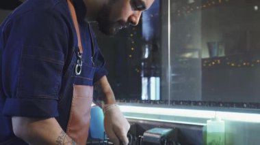 Odaklanmış, iyi bakımlı sakallı bir şef canlı domatesleri ustaca dilimliyor, canlı bir restoran mutfağında aşçılık uzmanlığını sergiliyor. Işıldayan bıçak taze ürünlerin arasında süzülür, tutkuyu ve hassasiyeti somutlaştırır.
