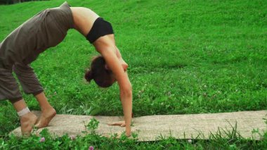 Genç bir kız, zorlu bir yoga pozu vererek inanılmaz esnekliğini sergiliyor. Sırtını zarif bir şekilde canlı yeşil bir zemine yaslıyor. Onun dingin ifadesi ve atletik kıyafeti onun sağlığına ve güzelliğine olan bağlılığını vurguluyor.