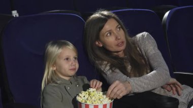 Güzel bir kadın ve tapılası küçük kızı pofuduk sinema koltuklarında oturup tereyağlı patlamış mısırları yerken bir filme dalmışlar. Bu iç açıcı sahne aile bağlarının özünü yakalar, paylaşılan anların neşe ve heyecanını gözler önüne serer.