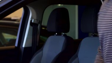 Şık, bakımlı sakallı genç bir Afro-Amerikan adam galerideki lüks bir arabanın içinde oturmuş heyecan saçıyor. Güneş ışığı pencereden içeri girerken, memnuniyetini ve onayını gösteren neşeli bir baş parmak hareketi yapıyor.