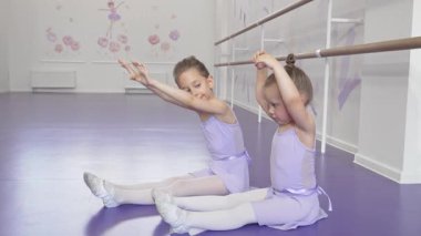 İki küçük sevimli balerin, parlak bir dans stüdyosunda zarif bir şekilde esniyorlar. Yumuşak lavanta rengi taytları, parlak mor zeminle çok güzel zıt düşüyor. Bu büyüleyici sahne çocukluk sevincini ve bale disiplinini yansıtıyor.