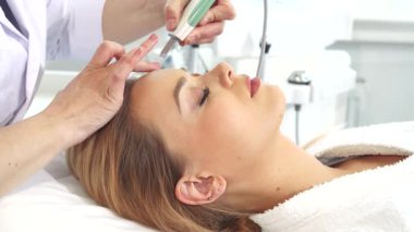 Çekici genç bir kadın, yetenekli bir güzellik uzmanlığı ile alnında ultrasonik bir ovalayıcı süzülerek teninin parlaklığını arttırırken rahatlıyor. Bu rahatlatıcı yüz tedavisi derin bir temizlik ve tazeleme vaad ediyor, cildini pürüzsüz ve pürüzsüz kılıyor.