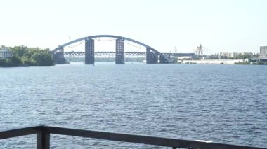 Genç bir kadının sağdan girip boynunu havluyla silerken nefes kesici bir nehir kenarı sahnesi ortaya çıkıyor. Uzun siyah saçları at kuyruğu gibi geriye çekilmiş, düşünceli bir şekilde ışıldayan suya ve kentsel ufka bakıyor, bir an için...