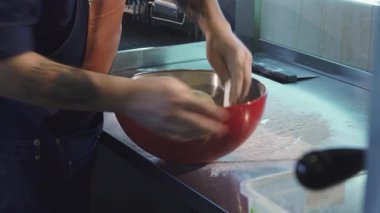 Profesyonel üniformalı odaklanmış bir erkek şef, un ve mutfak aletleriyle çevrili canlı bir mutfakta ustaca hamur yoğurur. Elleri titizlikle hareket ediyor. Lezzetli ekmek ya da pizza kreasyonlarına hazırlanırken pişirme sanatını somutlaştırıyor.