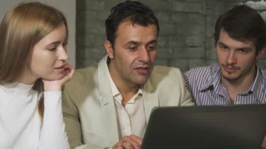 Olgun bir iş adamı genç iş arkadaşlarıyla dinamik bir tartışmaya girer, hepsi modern ofis ortamındaki bir dizüstü bilgisayara odaklanır. Sahne takım çalışması ve yenilik yayıyor, deneyimin ve yeni fikirlerin karışımını işbirlikçi bir şekilde gösteriyor.