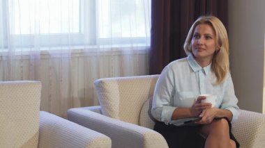 Neşeli bir kadın şık bir sandalyeye rahatça oturur, bir elinde uzaktan kumandayla ve diğer elinde dumanı tüten bir fincan kahveyle, zahmetsizce televizyon kanallarında geçiş yapar. Otel odasının ılık atmosferi yumuşak perdeler ve davetkar dekorlarla süslenmişti.