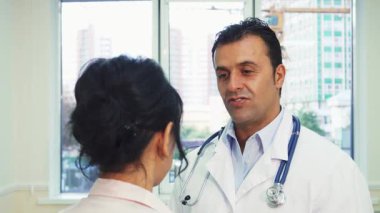 Doğal ışıkla dolu parlak bir ofiste, kendine güvenen bir doktor genç bir kadınla değerli sağlık tavsiyelerini paylaşır. Cana yakın konuşmaları dostça bir jest ile sonuçlanıyor. Omzunu nazikçe okşuyor, güven ve özen duygusunu geliştiriyor.