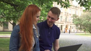 Çekici bir çift öğrenci, dizüstü bilgisayarlarına dalmış bir bankta otururken fikirlerini paylaşıyorlar. Yakışıklı sarışın adam canlı bir şekilde güzel kızıl saçlı sınıf arkadaşıyla konuşuyor. Etrafı yemyeşil ve kampüs hayatının canlı atmosferiyle çevrili.