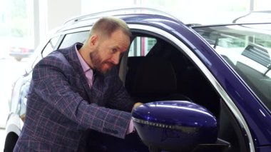 Sakallı iyi giyimli bir adam çarpıcı mavi bir arabanın yanında duruyor, elini yan ayna boyunca yavaşça süzülüyor. Detaylara olan keskin gözü araç tasarımına olan hayranlığını yansıtıyor. Mükemmel bir tarz karışımı sergiliyor.