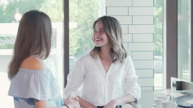 Neşeli bir kadın parlak, davetkar bir kahve dükkanında arkadaşlarını sıcak bir gülümsemeyle karşılar, kahkaha ve arkadaşlıkla dolu canlı bir atmosfer yaratır. Bu keyifli sahne, dostluğun ve rahatlamanın özünü yansıtıyor, hikayelerini paylaştıkça.
