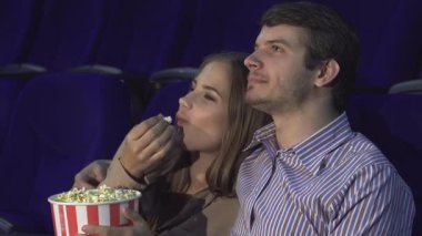 Sevimli bir çift, samimi bir sinemada oturup romantik komedi izlerken kahkahalarını paylaşıyor. Ellerinde patlamış mısırla, neşeli ifadeleri mutluluk saçıyor, sevgi ve bağdan oluşan hoş bir atmosfer yaratıyor.