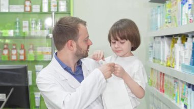 Dost canlısı bir eczacı kameraya ışık tutarken küçük tatlı bir çocuk da şekerlerle dolu bir alışveriş çantası tutuyor. Bu iç açıcı sahne tüketiciliğin özünü ve hizmet ile memnuniyet arasındaki hoş bağı yakalar.