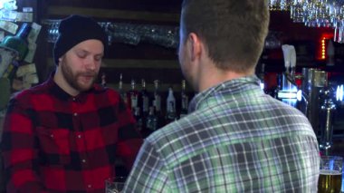 İki Kafkasyalı arkadaş, kırmızı kareli gömlek ve siyah bere takan bir adamla modern bir barda ateşli bir sohbete giriştiler. Diğeri, kahverengi saçlı, bar tezgahının yanında rahat ve neşeli duruyor.