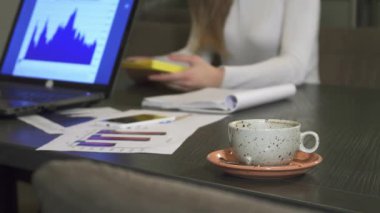 Benekli bir kahve fincanının yakın çekimi pembe bir fincan tabağının üzerinde yer alırken, iş adamları bir yönetim kurulunda işbirliği yaparak dizüstü bilgisayardaki grafikleri analiz ediyorlar. Atmosfer, strateji ve fikirleri tartışırken odaklanma ve kararlılıkla doludur.