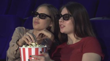 Sıcak bir sinema salonunda, üç boyutlu gözlük takan iki genç kadın büyüleyici bir filmle ilgili düşüncelerini paylaşıyorlar. Ellerinde büyük çizgili bir patlamış mısır kovası ile, anın tadını çıkarırlar, kahkahalar ve heyecan yüzlerini aydınlatır.