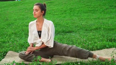 Güzel genç kadın yemyeşil çimlerle çevrili doğal bir paspasın üzerinde rahat bir şekilde oturmaktadır. Neşeli gülüşü huzur ve pozitiflik saçıyor, sağlıklı bir yaşam tarzı ve iç huzurun özünü somutlaştırıyor.