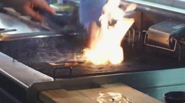 Yakından çekilen bir fotoğraf, lezzetli bir domuz bifteğini ustalıkla ızgarada yakalar, etin etrafında alevler içinde dans eder, baştan çıkarıcı bir aşçılık gösterisi yaratır. Canlı ateş, cızırdayan domuzun zengin kokusunu güçlendirir. Ağız sulandıran bir yemek sözü verir.