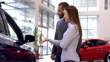 Çekici, ırklar arası bir çift, parlak, modern bir bayilikte, yeni ve şık bir aracı inceliyor. Güzel beyaz kadın coşkuyla arabayı işaret ederken, onun yakışıklı Afrikalı Amerikalı partneri kapıyı açıp, paylaştıklarını gösteriyor.