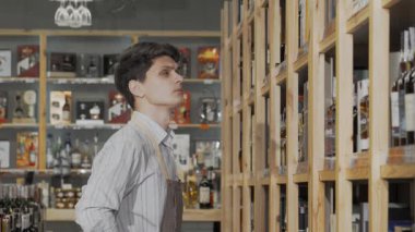 Odaklanmış genç bir şarap imalatçısı, mağazasındaki düzgün düzenlenmiş raflarda özenle bir dizi şarap şişesi düzenliyor. Bu sahne, şarap yapma sanatındaki adanmışlık ve uzmanlığın özünü yansıtıyor, canlı bir atmosfer sergiliyor.