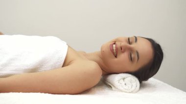 Yumuşak beyaz bir havluya sarılmış sakin bir beyaz kız masaj masasında uzanmış, rahatlama ve onaylama yayıyor. Onun barışçıl ifadesi ve kapalı gözleri, huzurun özünü somutlaştıran, mutluluk dolu bir kaçışa işaret ediyor.