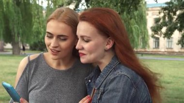 Biri çarpıcı kızıl saçlı, diğeri sarışın iki genç kadın, lüks bir parkta akıllı bir telefona göz gezdirirken mutlu bir şekilde sohbet ediyorlar. Kahkahaları havayı dolduruyor, keyifli anları paylaşıyorlar, canlı yeşillikler ve...