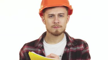 Ciddi bir genç sakallı erkek mimar, ekose gömlekli ve turuncu şapkalı, dikkatle parlak sarı bir not defterine notlar yazıyor. Bu görüntü, inşaat endüstrisindeki adanmışlık ve profesyonelliğin özünü yansıtıyor.