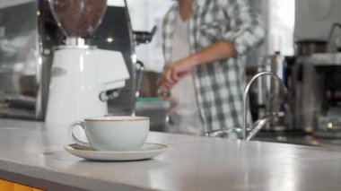 Güzel bir el yapımı kahve fincanı, yetenekli bir barista hareketli kahve dükkanında lezzetli sıcak içecekler hazırlarken tezgahın üzerinde davetkâr bir şekilde oturur. Sıcak atmosfer taze demlenmiş kahvenin zengin aromasıyla dolu, rahat bir şehir yaratıyor.