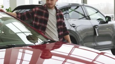 Şık ekose gömlekli neşeli sakallı bir adam modern bir galeride yeni arabasını kucaklarken zevkle ışıldıyor. Bu canlı sahne, sahipliğin heyecanını ve yeni maceralara atılmanın heyecanını yakalıyor.