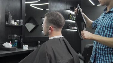 Şık bir berber dükkanında, yetenekli bir berber erkek müşterisine aynasını sunar, o da yeni saç kesimini hevesle inceler. Atmosfer modern ve canlı, tımar sanatının ve yeni bir görünümün zevkini sergiliyor.