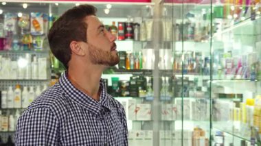 Sakallı neşeli esmer bir adam elinde kocaman bir gülümsemeyle elinde bir kağıt paketle dolu bir eczanede duruyor. Baş parmak hareketi pozitif enerji yayıyor, müşterileri etrafındaki sağlık ürünlerini keşfetmeye davet ediyor.