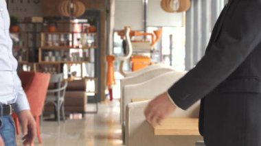 Düşük açılı dinamik bir çekim, iki iyi giyimli iş ortağını sıkı bir tokalaşma içinde yakalar ve işbirliğini sembolize eder. İçerideki davetkar kafe, rahat koltukları ve camdan içeri yayılan doğal ışıklarıyla, mükemmel bir yer hazırlıyor.